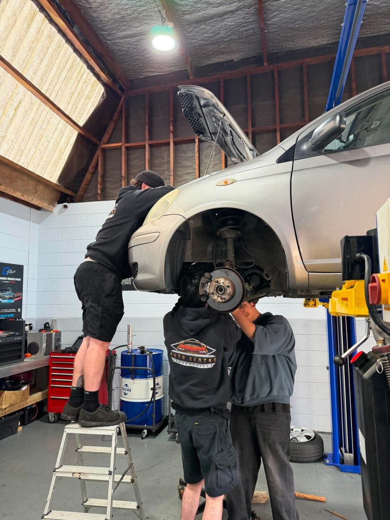 The team working on a silver hatchback raised on a hoist in the Johnsonville workshop